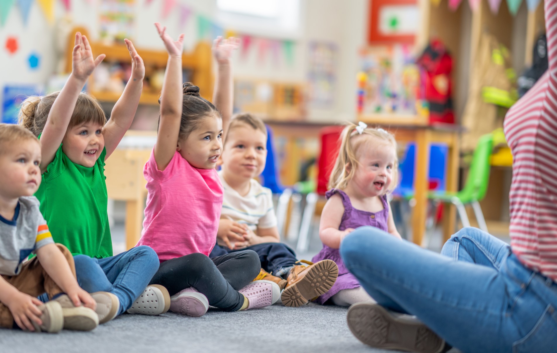 seated group of children listening to their teacher and raising their hands