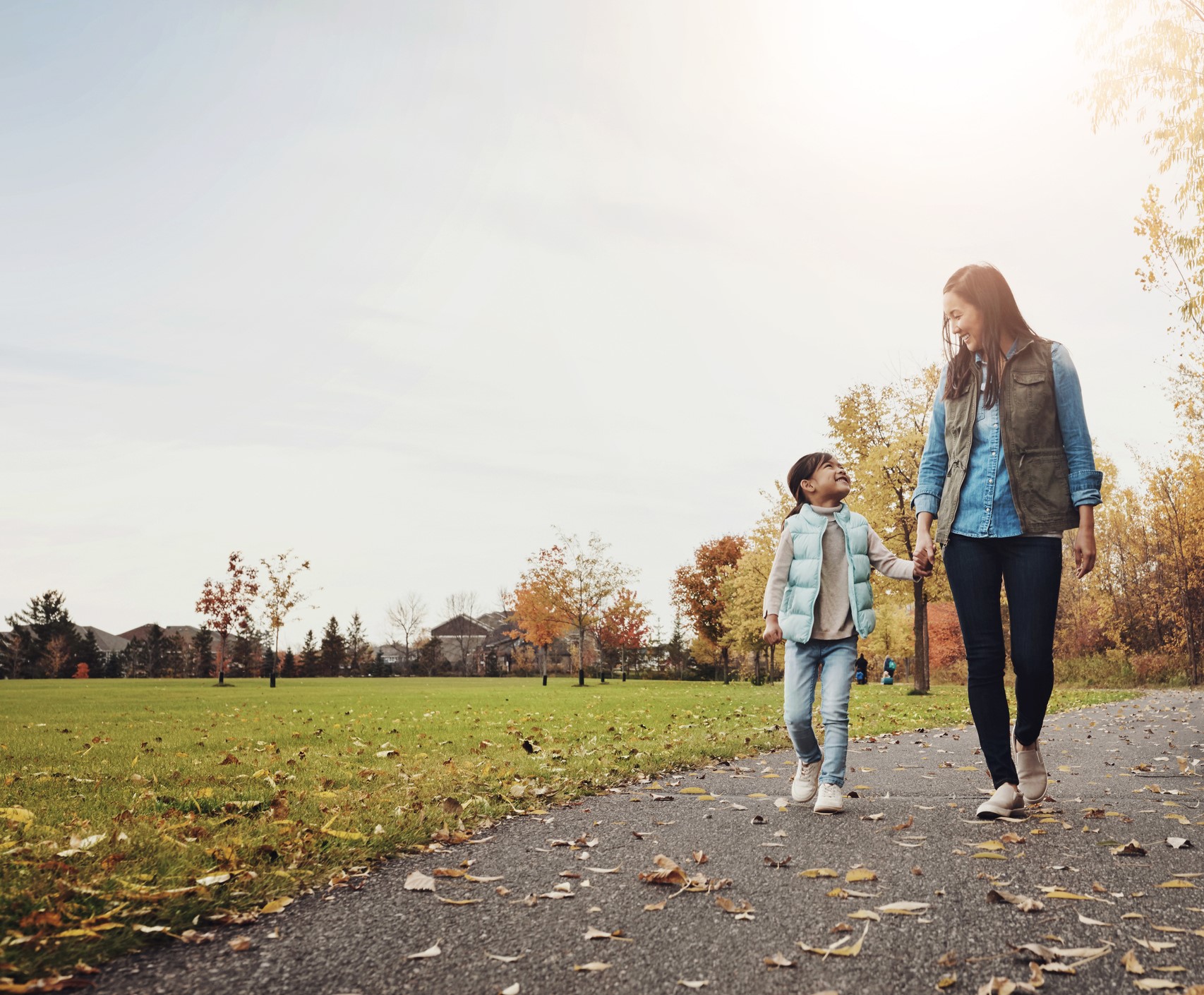 Smiling mother and daughter holding hands and looking at each other while walking in the park