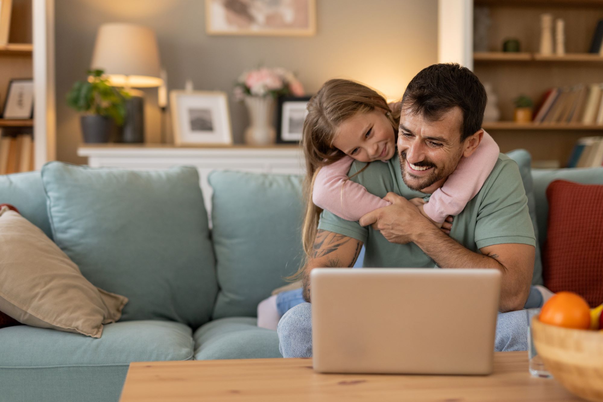 smiling young dad on his computer with his daughter's arms around him
