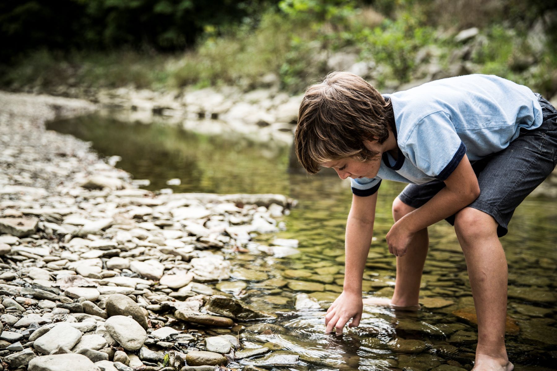 boy stoops to collect rocks in a creek