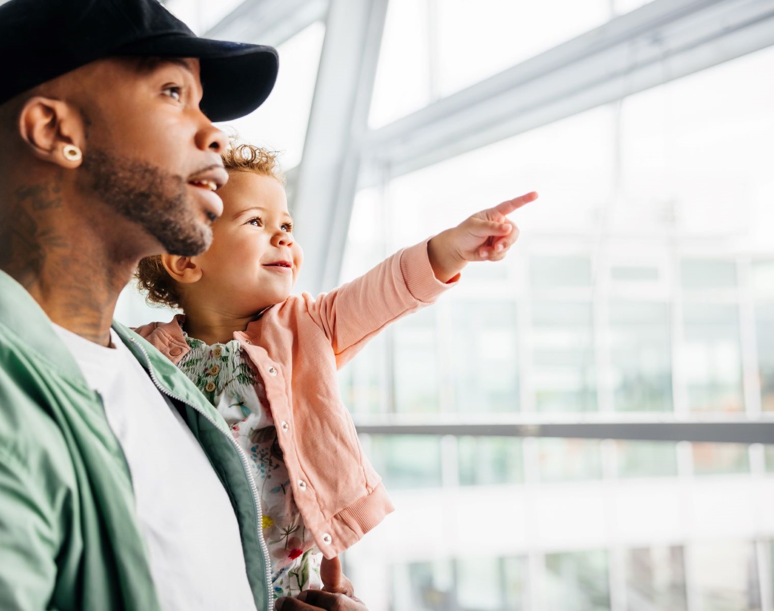young african-american father holding his young daughter who is pointing out a window