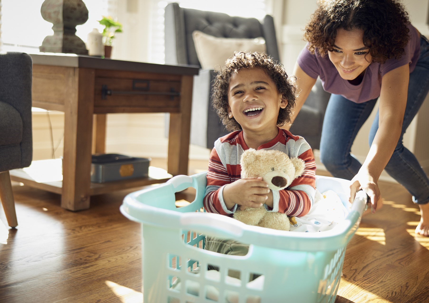 laughing boy being pushed in a laundry basket by mom