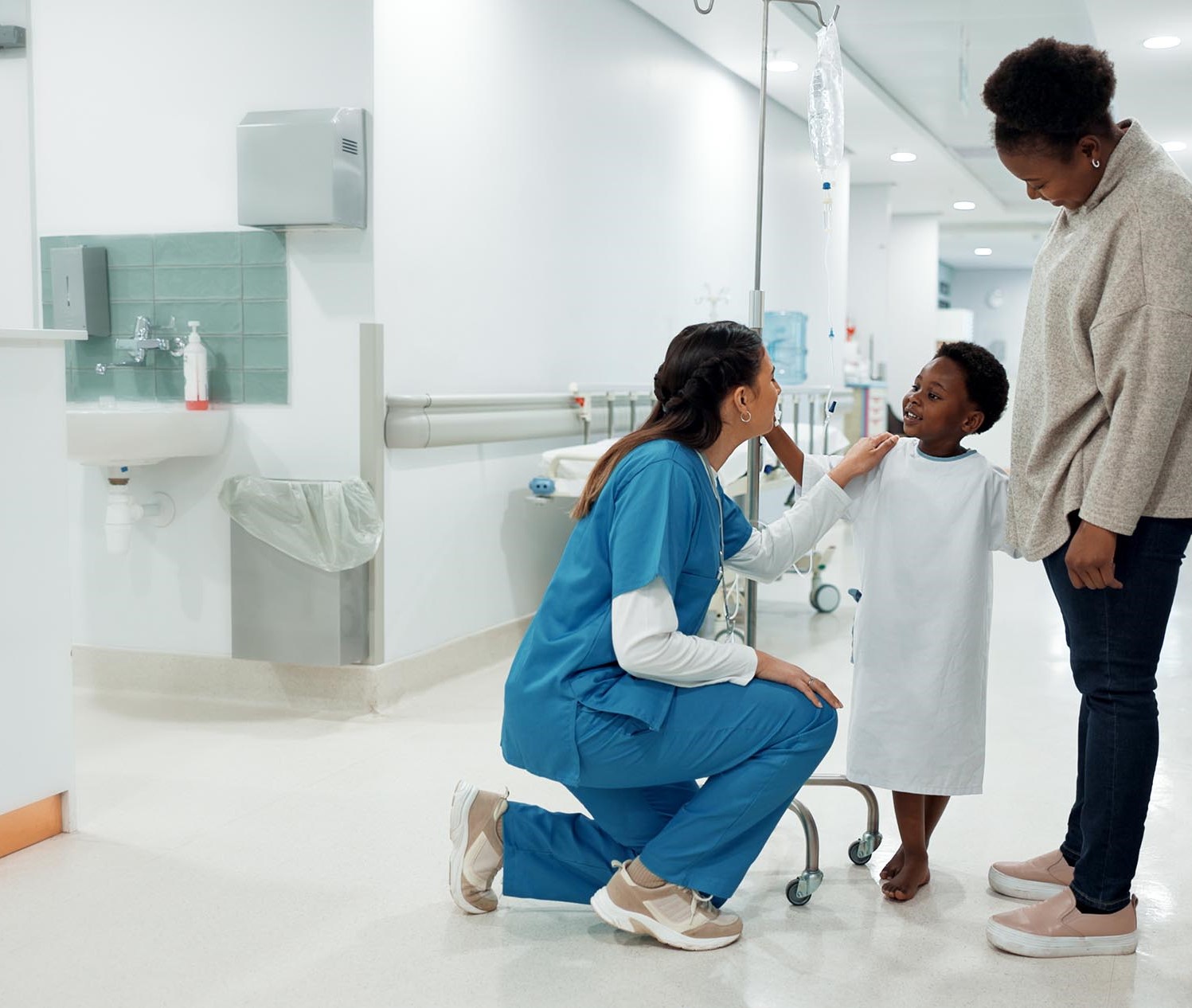 young boy in a hospital gown with his mother is being reassured by a nurse