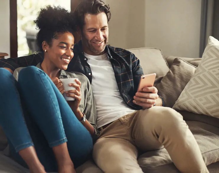 male and female couple sitting comfortably together on the sofa looking at his phone