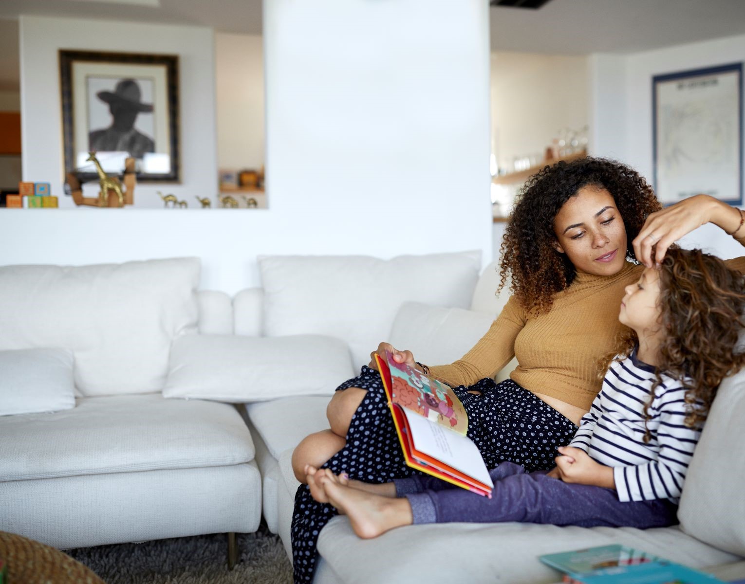 girl sits on the couch with mom next to her brushing her hair back from her face
