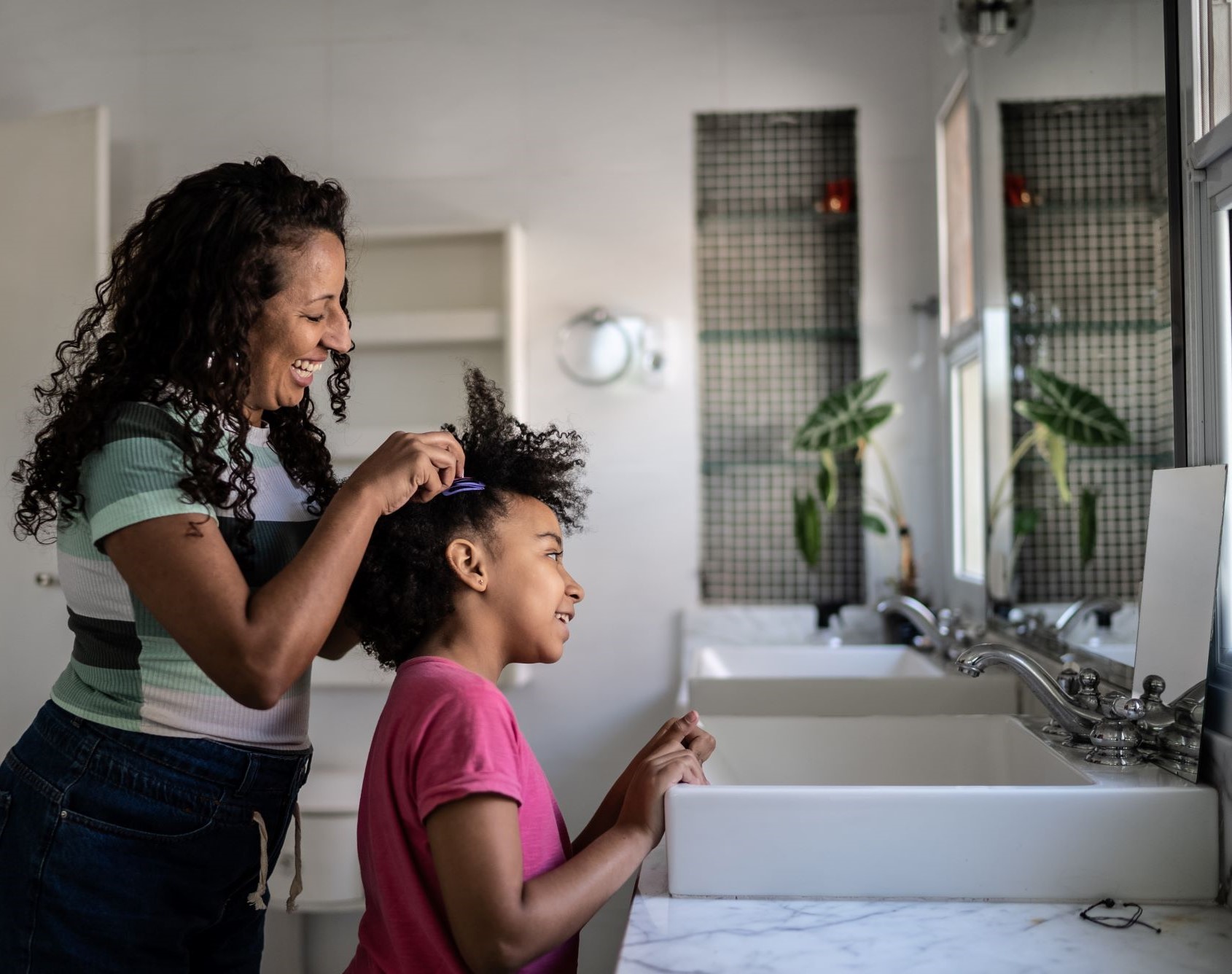 mother fixing her daughter's hair in front of the bathroom mirror