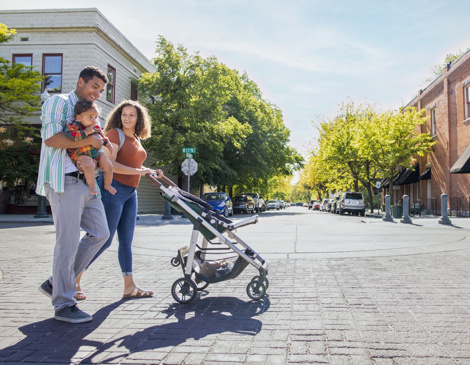 young mixed-race couple with baby and stroller walking in the sunshine on an urban street