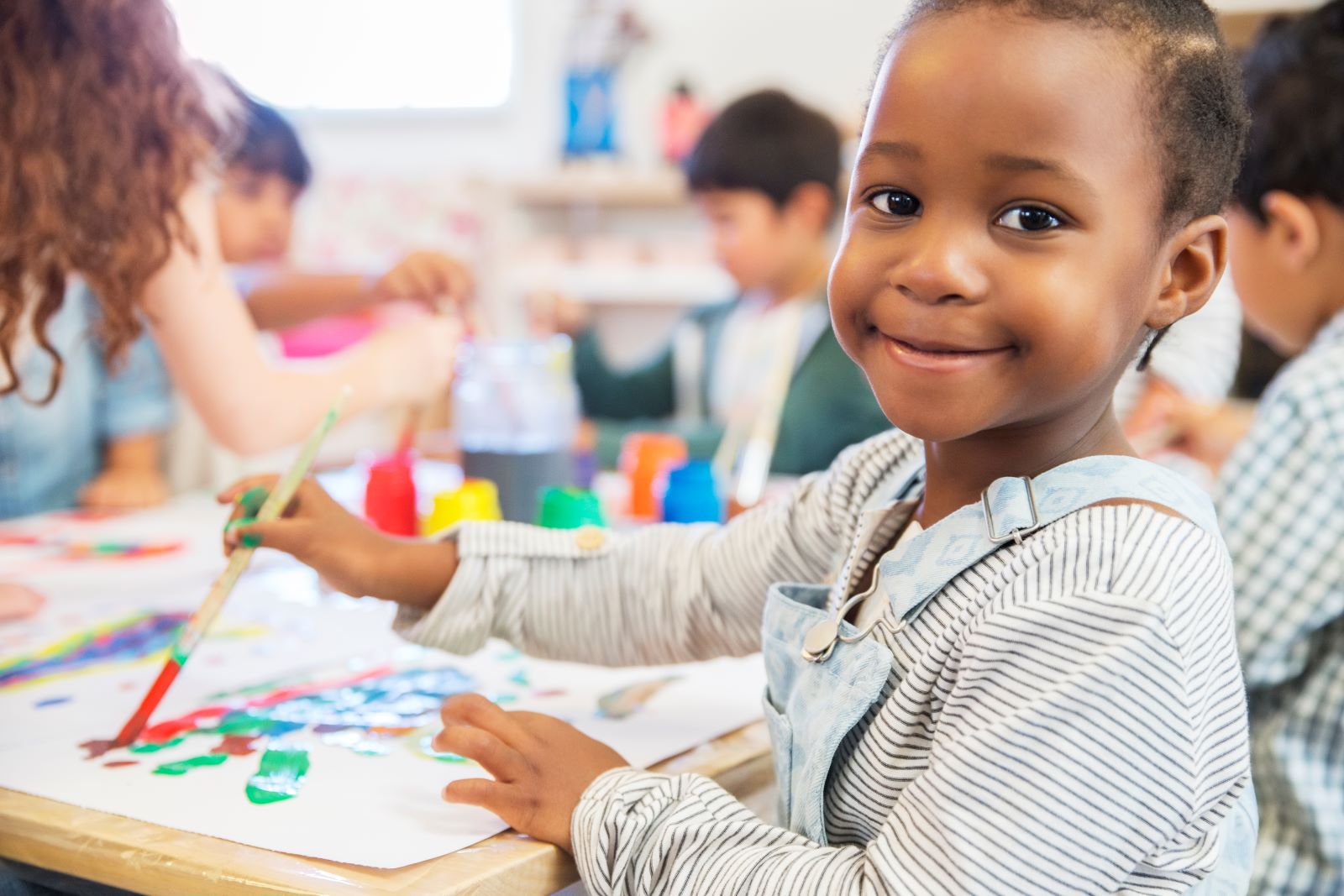 little girl painting a picture and smiling at the camera