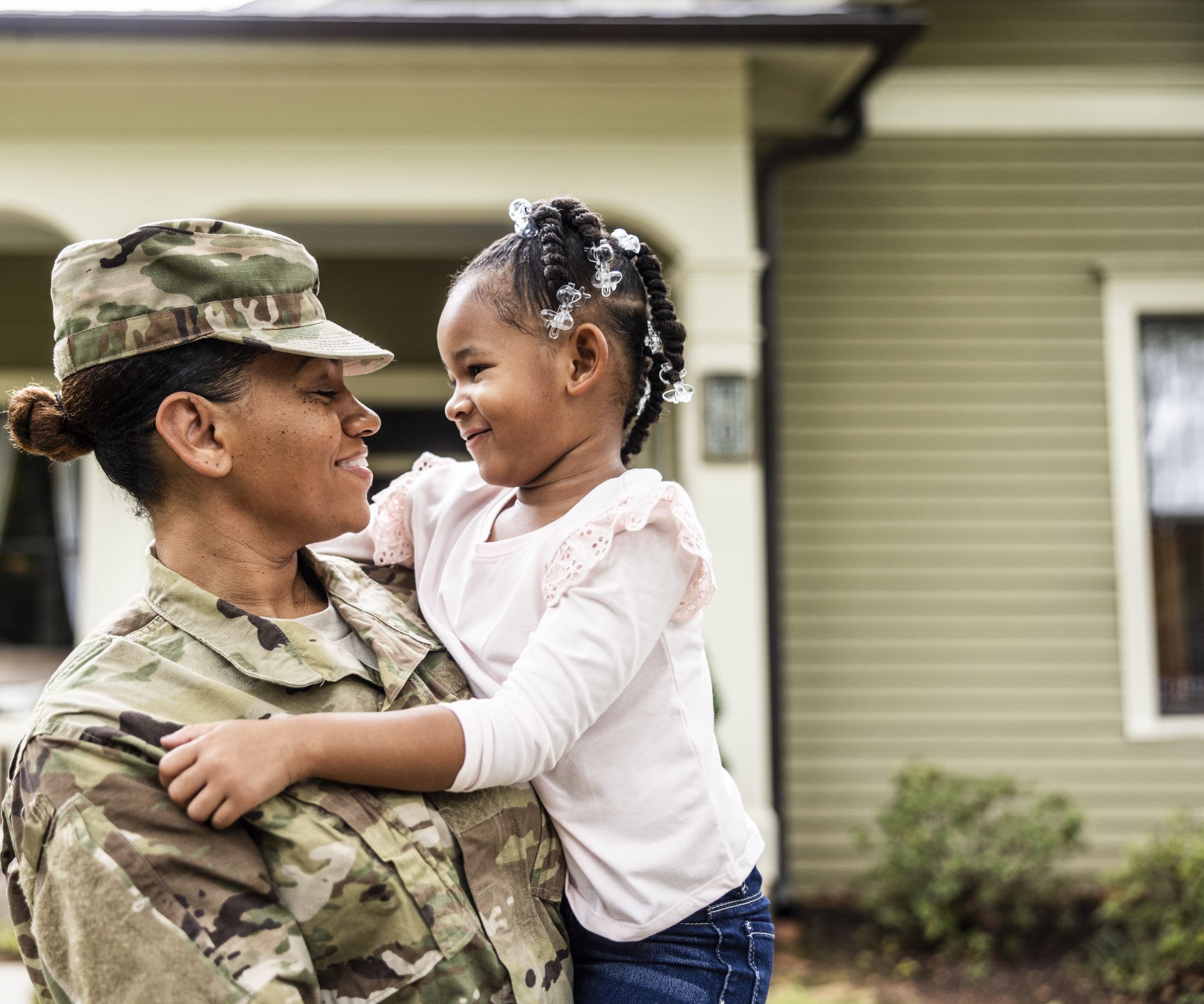 military mom smiling at her young daughter in her arms outside front door