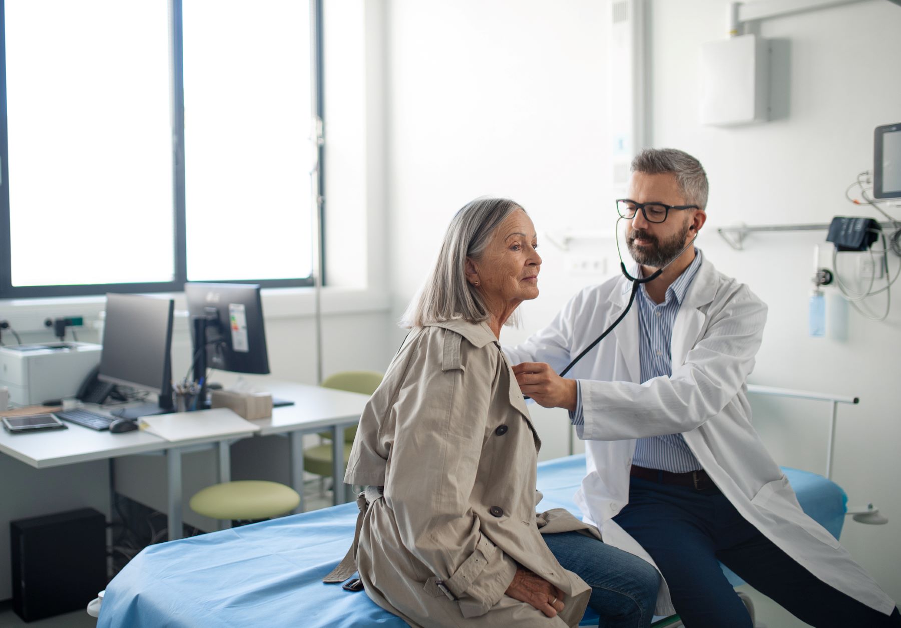 male doctor listens to older female patient's heart with his stethescope