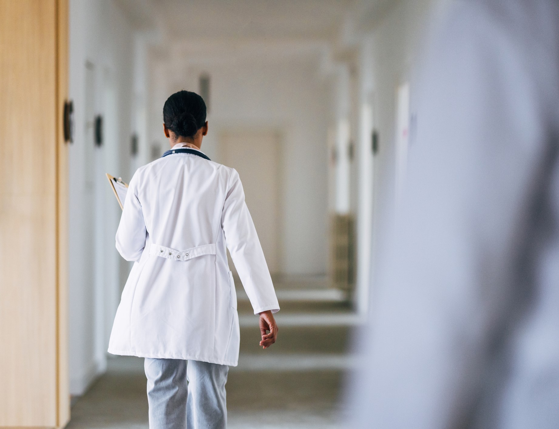 Rear view of a doctor walking down a hallway holding some papers